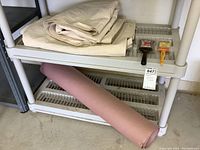 Two folded beige canvas drop cloths on a shelf with a large roll of brown kraft paper underneath, and two paint brushes beside them.