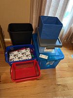 Photo showing two large plastic tubs with lids, two plastic baskets (one blue, one red), and a blue fabric cube container stacked on the blue tub.