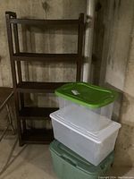 Photo showing the brown plastic shelving unit and three clear plastic storage bins stacked in front of it, each with different colored lids