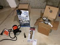 Flotec utility pump with packaging for valve and boxed pressure gauge plus small fitting on basement floor.
