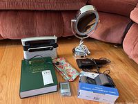 Full lot items on floor including mirror, radio, hair dryer, weights, colorful cosmetic bag, medical dictionary, and small digital device