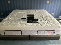 Full view of king size bed base with white mattress placeholder, remotes, manuals and power supply laid on top
