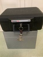 Closed view of the black SentrySafe 1100 security box stacked on top of the silver metal lockbox. Keys attached to SentrySafe lock.