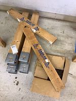 Photo shows two pairs of wooden sawhorses with metal brackets, two labeled wooden pieces, and a box of nails on the floor.