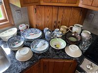Full set of Spode Christmas bowl, Folk Craft dishes, mugs, pitcher, colander, and stemless wine glasses arranged on a kitchen counter.