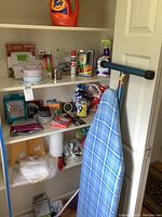 Wide view of shelves holding various cleaning supplies, thermostat, plumbing parts, and ironing board.