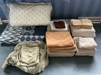Overview of towels, bedding, sheet set and quilts arranged on floor showing various colors and patterns.