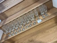 32 clear champagne glasses arranged in four rows on wooden steps, showing the full set.
