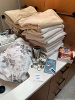 Photo showing stacked beige bath towels, decorative metal shower curtain hooks, a white shower curtain with floral design, and two books including 'Uncle Johns Bathroom Reader'.
