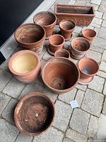 Overview of assorted outdoor clay pots arranged on pavement, showing a variety of sizes and shapes.
