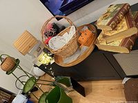 Photo showing decorative book-style storage boxes stacked, green metal plant stand, wicker basket with plates and small storage box, and a bamboo tray underneath.