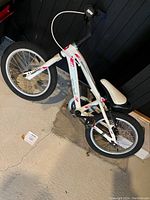 Full side view of the white kids Garneau bicycle showing frame, tires, seat, and handlebars on concrete floor.