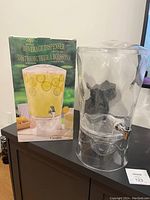 Large clear plastic beverage dispenser shown with original box featuring beverage image.