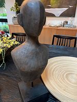 Wooden bust sculpture showing dark wood tone and modern abstract style on black rectangular base next to wooden tray.