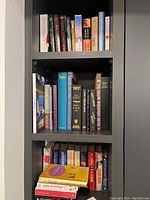 Books on three shelves showing varied titles and genres, mixed hardcover and paperback editions.