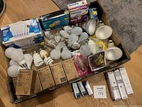 Box with assortment of LED bulbs in packages, loose bulbs, and some specialty bulbs from brands Eccomsmart and Philips.
