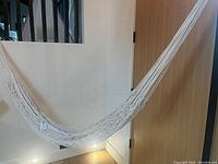 Photo showing full view of white macrame hammock hung indoors, displaying its woven cotton rope netting and comfortable curved shape.