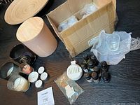 Overview of candles, glass candle holders, essential oil bottles, and candle accessory items on black surface with a wooden plate partially visible