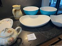 Overview of all items on black countertop including ceramic pitcher, turquoise bowls, white platters, and floral porcelain teapot.