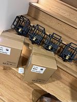 Six new Maxim wall sconces shown on wooden stairs along with packaging boxes labeled Maxim Lighting 10241BKSBR.