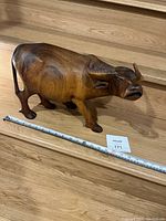 Side view of the solid wood water buffalo statue placed on a wooden surface with measuring stick showing size.