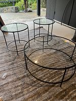 Three piece coffee table set with oval coffee table and two round end tables, showing full set on a carpet.