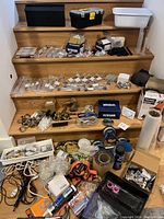 Wide photo showing all items arranged on wooden steps including cabinet pulls, latches, hooks, toolbox, cords, and packaging materials