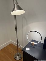 View of entire adjustable stainless steel floor lamp with conical shade and circular LED touch bedside lamp on black table.