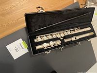 Open black hard case showing the silver Gemeinhardt 2SP flute in three sections inside with black plush lining and a cleaning rod.