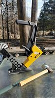 Side view of DeWalt air flooring nailer and wooden mallet on glass table outdoors.
