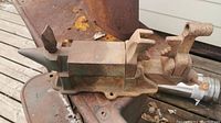 Small iron anvil with pointed horn and attached adjustable vise clamp.