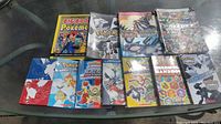 Top view of all 11 Pokemon handbooks arranged on a glass table showing variety of cover arts and editions.