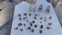 Photo of assortment of brass miniatures on white paper on table, showing miniature furniture and various household shaped items.