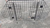 Full view of black metal wire grid car pet gate with latch and legs for stability.