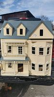 Front view of the cream-colored vintage dollhouse showing porch and balcony with detailed architectural features.