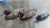 Top and front view of three wooden duck decoys on glass table showing their colors and sizes