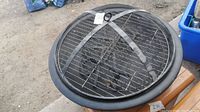 Top view of round fire pit with mesh lid in place, showing the full circular metal edge and mesh surface.