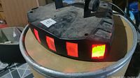 Triangular black DJ stage light showing red illuminated panels on one side, dusty surface.