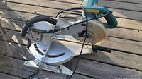 Front angled view of saw on wood deck showing blade, base, and handle.