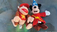 Photo showing front view of Diddy Kong and Mickey Mouse plushies on a textured surface.