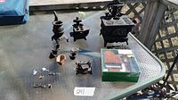 Photo showing the entire lot of miniature cast iron household items on a glass table outdoors under sunlight. Includes mini stoves, sewing machine, keys and other small items and a boxed set of wooden miniatures.