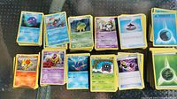Stacks of Pokemon trading cards showing front faces with different characters like Crobat, Eevee, Grotle, Paras, Corsola, and energy cards in various colors.