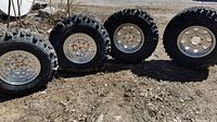 Four mud terrain tires mounted on polished aluminum beadlock-style wheels outdoors