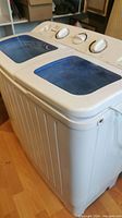 Side angle view showing white compact washing machine with blue translucent lids and control knobs.