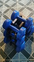 Three pairs of blue vinyl coated dumbbells arranged on a black plastic rack on tiled floor.