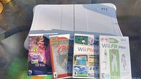Wii Balance Board with five Wii game cases surrounding it on a table.