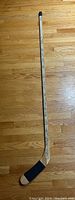 Full view of the signed wooden hockey stick lying on a wooden floor, showing black tape on the blade and numerous signatures along the shaft