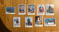 Front sides of nine Superman trading cards laid out on wooden surface showing various images of Superman and Christopher Reeve.