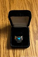 Top-down view of the Thunderbird ring in a black velvet box showing the silver ring face with turquoise stone and engraved design.