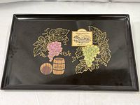 Full view of rectangular black tray with grape clusters, grapevines, wine barrels, and vintage wine label design on surface.